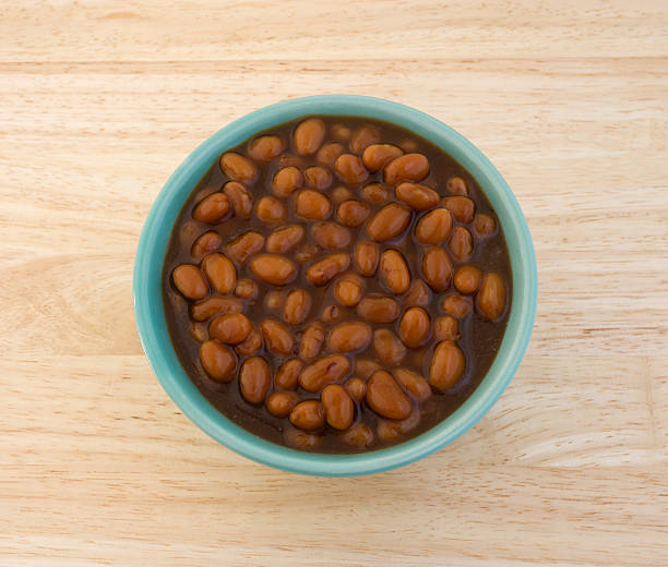 Top view of a bowl filled with country style baked beans on a wood table top.