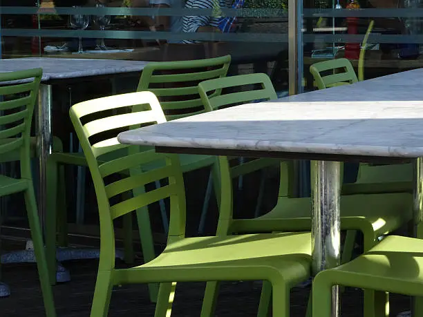 Photo showing some tables and chairs pictured outside a pavement cafe, with marble tabletops and bright green chairs.