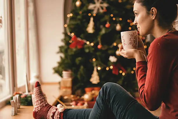 Photo of Young woman drinking tea by the Christmas tree