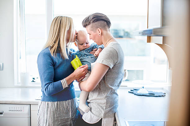 Loving young lesbian couple with baby in kitchen Loving young lesbian couple with baby in kitchen. Mother is kissing toddler in domestic room. Family of three is in brightly lit room. unknown gender stock pictures, royalty-free photos & images