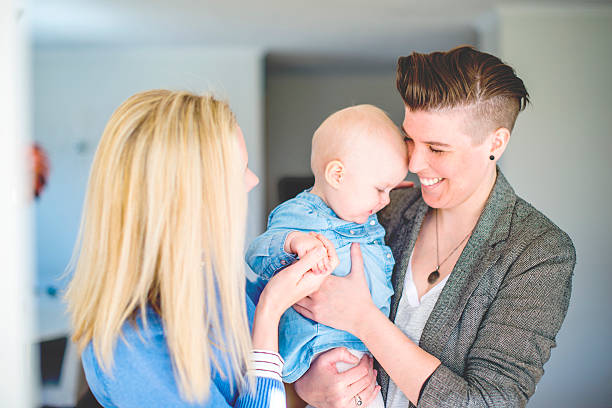 Young lesbian couple playing with baby at home Young lesbian couple playing with baby at home. Loving female partners with cute toddler in living room. Happy family of three. unknown gender stock pictures, royalty-free photos & images