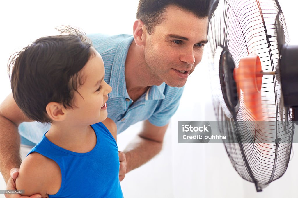 Padre e hijo delante de Ventilador de refrigeración. Día de calor - Foto de stock de Familia libre de derechos