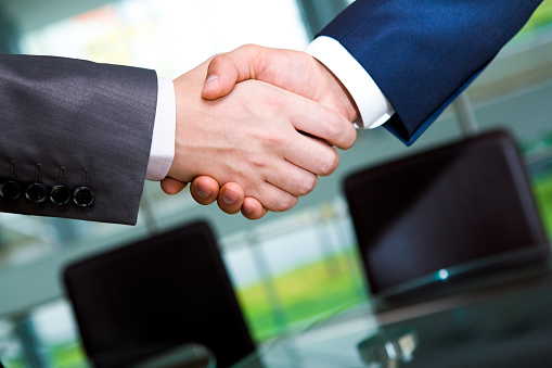Business people shaking hands while standing with colleagues after meeting or negotiation, close-up. Group of unknown businessmen and women in modern office. Teamwork, partnership and handshake concept, toned picture.