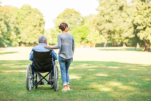 Senior man sitting on a wheelchair with caregiver stock photo