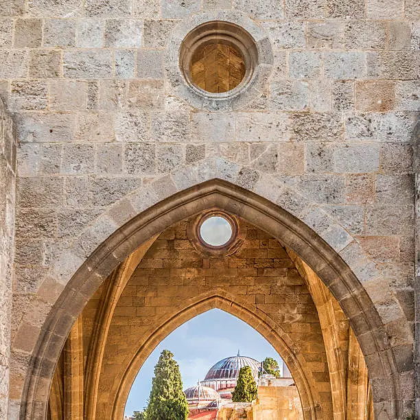 View from Palace of Grandmaster of Crusader order of Brothers Hospitaliers through sunlit entrance archway toward Suleyman Mosque. Faiths coexist peacefully on Rhodes in Greece.