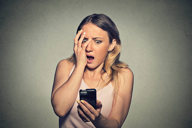 anxious scared girl looking at phone seeing bad news Closeup portrait anxious scared young girl looking at phone seeing bad news photos message with disgusting emotion on her face isolated on gray wall background. Human reaction, expression gasping stock pictures, royalty-free photos & images