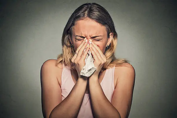 Brunette woman sneezing in a tissue blowing her runny nose