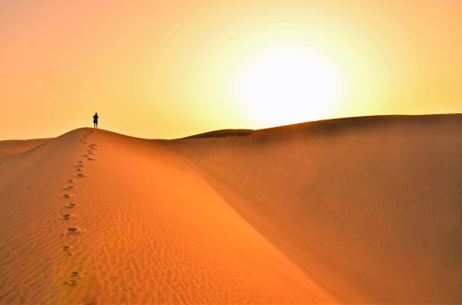 Three senior women walking, one barefoot on Wahiba desert sand in Oman. They are looking to the horizon, only sand, sky and there are some footprints in the sand.