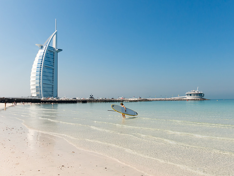 Dubai, United Arab Emirates - January 25, 2014: Woman with surf board on Jumeirah Beach with the luxury Burj al Arab hotel in the background