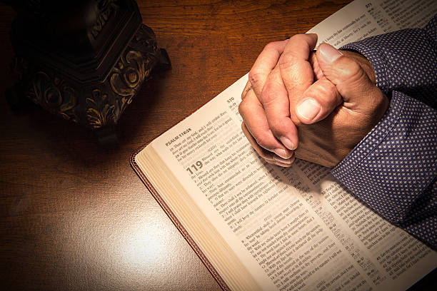 Praying hands on a bible Hands folded in prayer on a Holy Bible. baptist stock pictures, royalty-free photos & images
