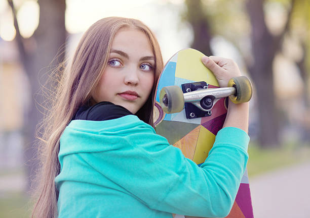 Portrait of beautiful teenage girl with skateboard in green park