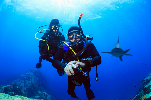 Closeup of two happy scuba divers underwater facing the camera showing the ok sign with the bright sunrays shining through the water surface behind them