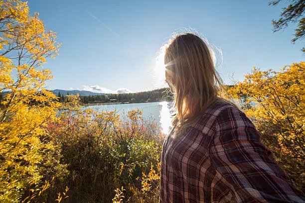 Young cheerful woman traveling in Canada takes a selfie portrait by the lake. Autumn season.