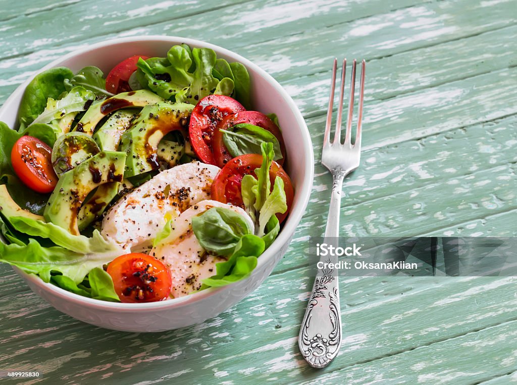 fresh salad with avocado, tomato and mozzarella fresh salad with avocado, tomato and mozzarella, in a white bowl on bright wooden surface 2015 Stock Photo