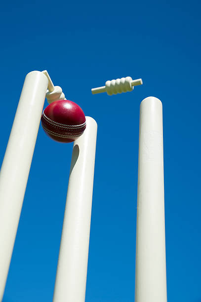 Cricket ball and stumps Cricket ball stumps the wicket as bails fly with blue sky cricket stump stock pictures, royalty-free photos & images