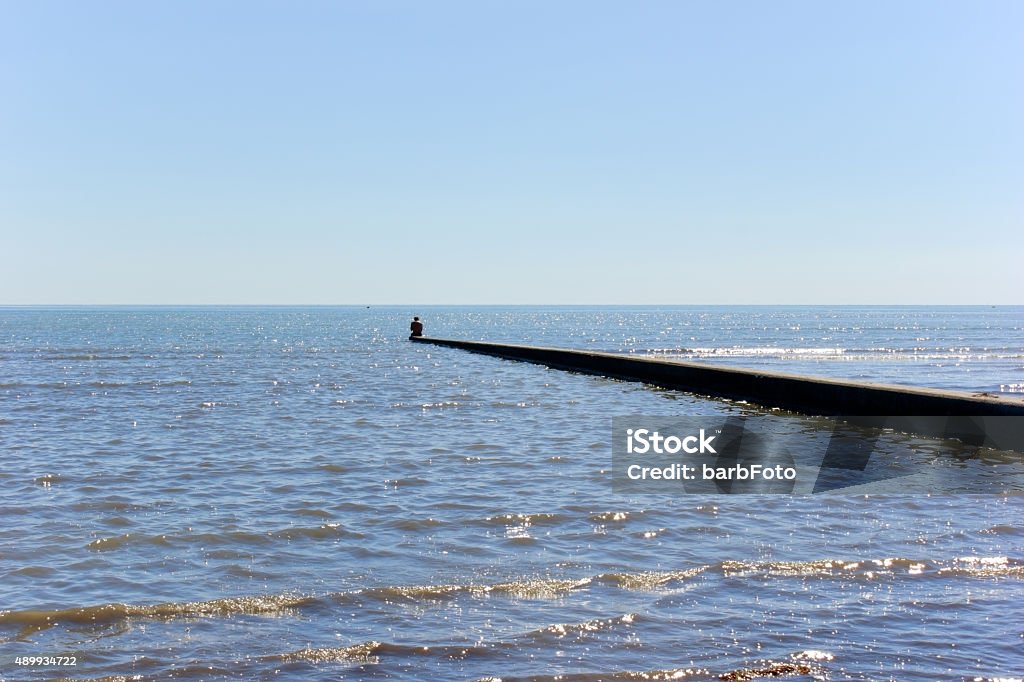 At the beach A man sitting on a sea wall in Grado, Italy. 2015 Stock Photo