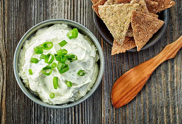 bowl of cream cheese with green onions and herbs, dip sauce on wooden table, top view