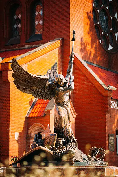 MINSK, BELARUS - May 20, 2015: Statue Of Archangel Michael With Outstretched Wings, Thrusting Spear Into Dragon near Red Catholic Church Of St. Simon And St. Helena On Independence Square