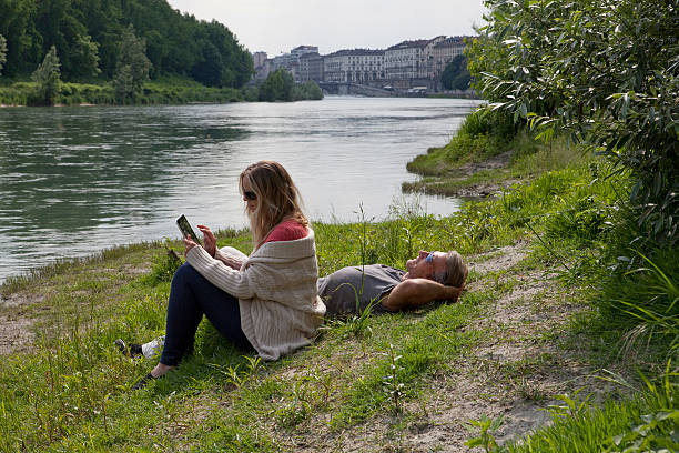 Woman uses digital tablet above river, man relaxes, Turin, Piedmont, Italy