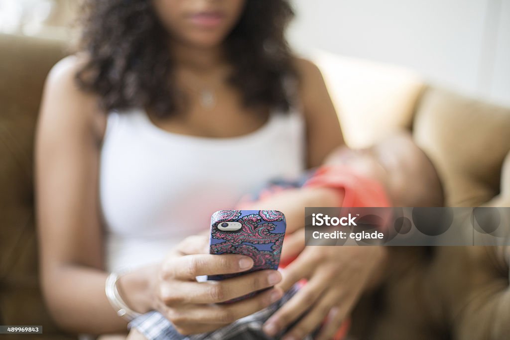 Young Mother On Cellphone Young African American mother using cell phone while baby sleeps Baby - Human Age Stock Photo