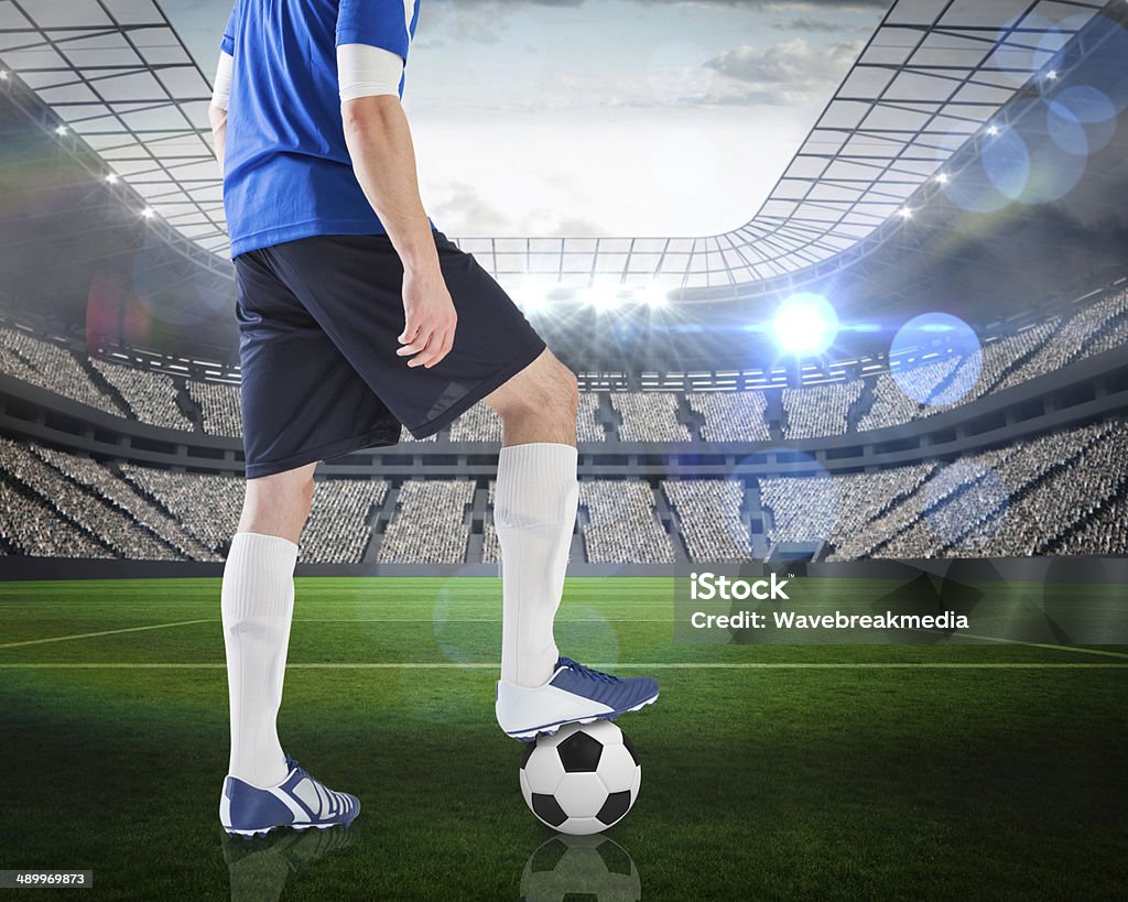 Football player standing with ball Composite image of football player standing with ball against large football stadium with lights Rear View Stock Photo