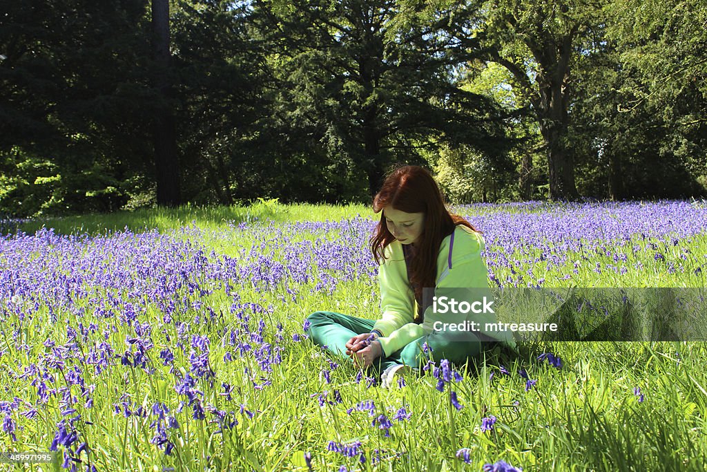 Girl with long hair sitting amongst woodland bluebells, dappled shade Photo showing a young girl with long red hair sitting amongst an abundance of flowering bluebells in a woodland garden, in the dappled shade. Agricultural Field Stock Photo