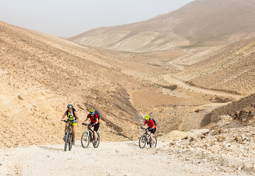 Three female mountainbikers are climbing in a steep section of a desert valley in Jordan.