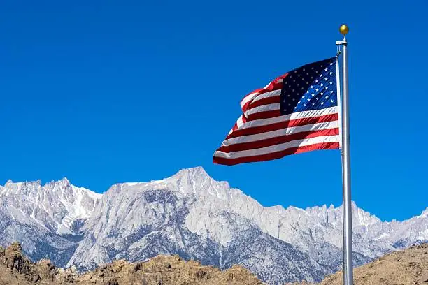 An American flag with Sierra Nevada mountain range in California in the background.