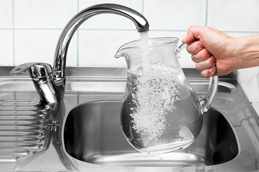 Hand holding a pitcher of water being poured from the kitchen faucet.