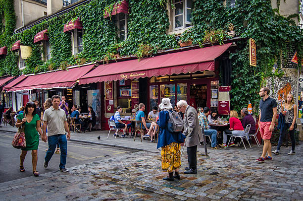 Paris, France - August 16, 2015: Marais street scene with older couple walking along Rue Hospitalières St. Gervais in front of Chez Marianne, a popular restaurant in the historic district of Marais.