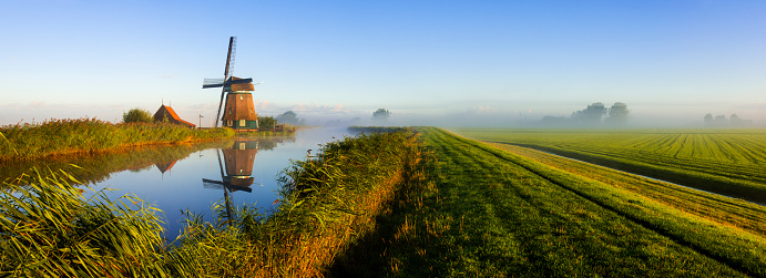 Panoramic image of a windmill along a canal during a hazy early morning. Location is polder Menningweer near Grootschermer, Netherlands.