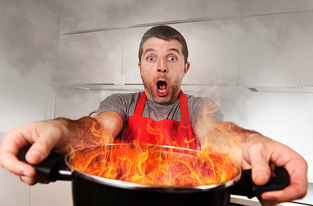 inexperienced home cook holding pot burning fire in panic stress stock photo