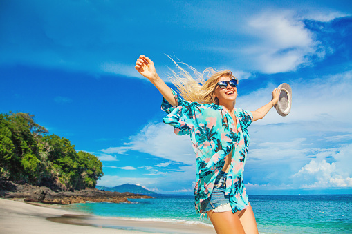 beautiful women in hawaiian shirt and jeans shorts jiumping on a background of tropical beach