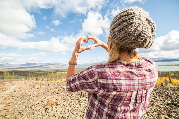Young cheerful woman enjoying nature in Autumn season. She is making a heart shape with her hands.