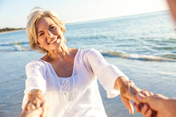 szczęśliwy starsza para spaceru trzymając ręce na plaży - senior couple senior adult walking action zdjęcia i obrazy z banku zdjęć