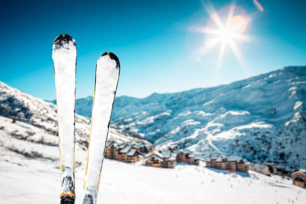 Snowcapped skis on the top of ski slope. Mountain ski village in the background.