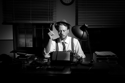 Retro reporter working late typing on a typewriter and smoking a cigarette.