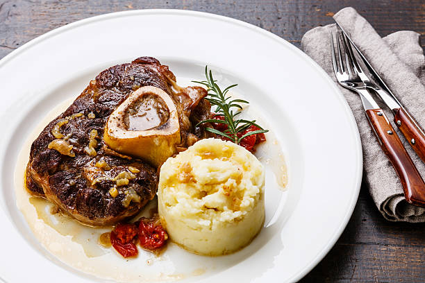 Ready-cooked Osso buco Veal shank with mashed potatoes on plate Ready-cooked Osso buco Veal shank with tomatoes and mashed potatoes on white plate on wooden background ossobuco stock pictures, royalty-free photos & images