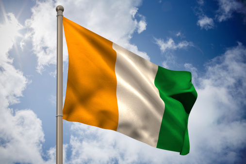 Ivory coast national flag on flagpole against bright blue sky with clouds