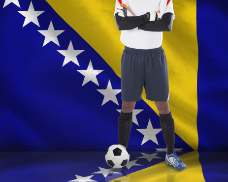 Goalkeeper in white looking at camera against digitally generated bosnian flag