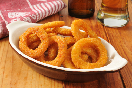 A serving of golden onion rings with beer on a rustic wooden bar counter