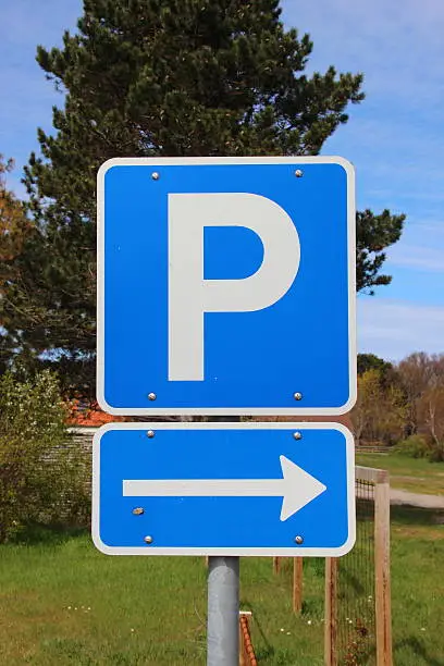 Blue parkinglot sign with right arrow and sky in background