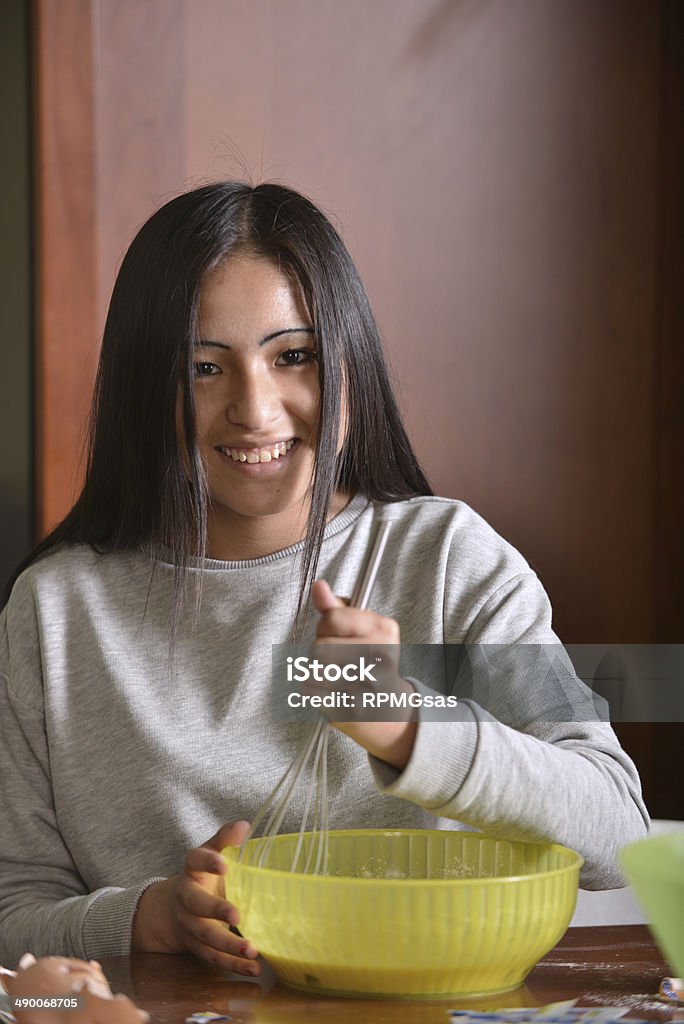 Hispanic teenager preparing a cake An hispanic teenager is preparing a cake in a bowl in the kitchen 14-15 Years Stock Photo