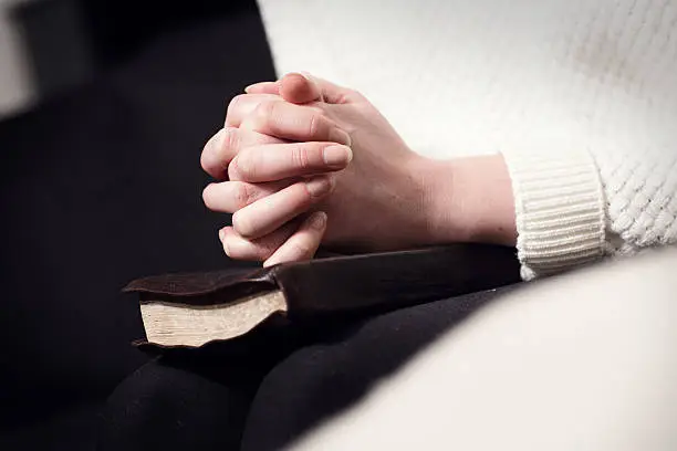 Photo of Praying woman folding hands over bible