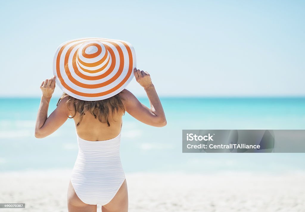 young woman in hat standing on beach. rear view Young woman in hat standing on beach. rear view Women Stock Photo