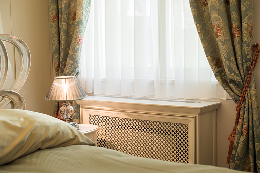 Wooden cover for radiator in bedroom interior