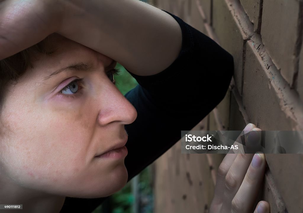 Woman in depression A woman in a very depressed mood stands near the brick wall. 2015 Stock Photo