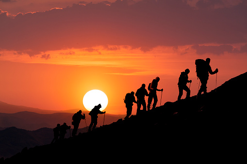 Silhouettes of hikers climbing the mountain at sunset. 