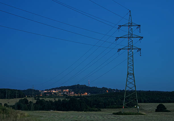 High power line pylons are intended to electrically lighted city in the background. Rural landscape in the evening.