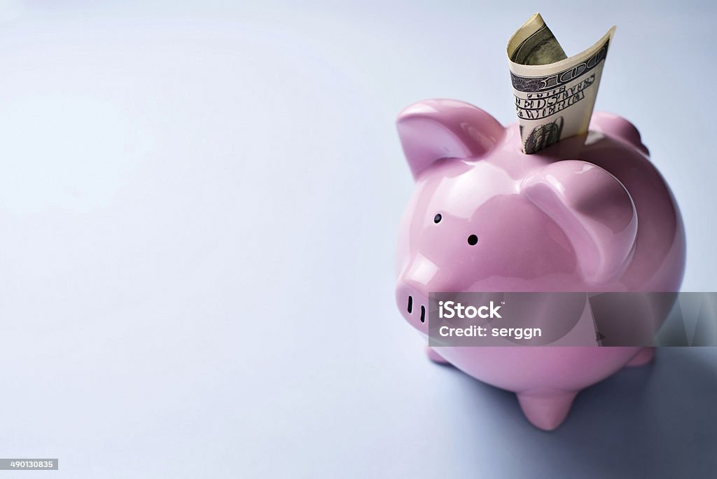 Pink piggy bank with a dollar bill in the slot High angle view of a pink ceramic piggy bank with a dollar bill in the slot over a grey background with copyspace Aspirations Stock Photo